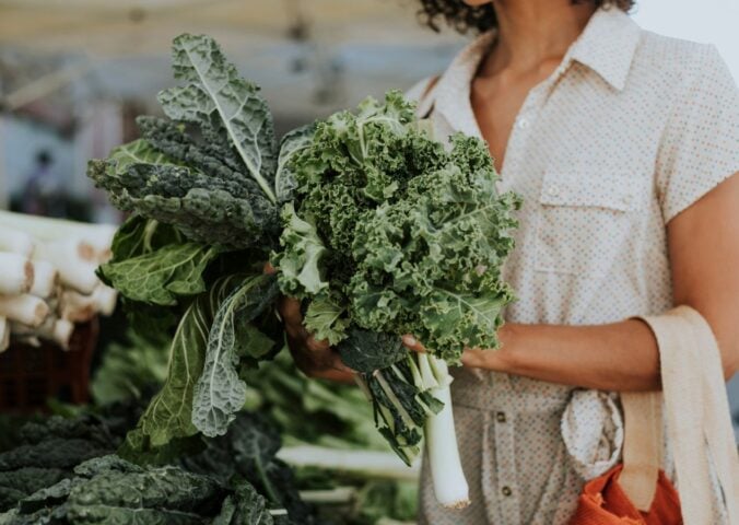 Photo shows a woman shopping and holding a large bunch of fresh kale, which is one of the top sources of plant-based calcium