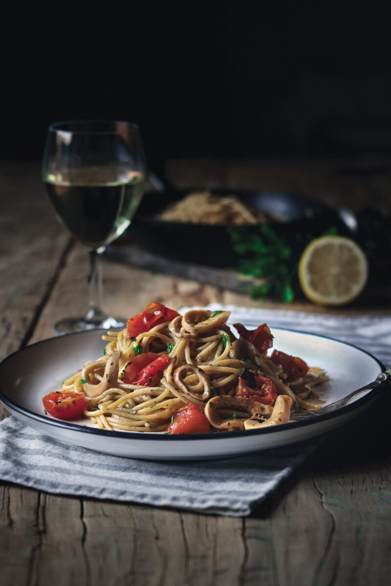 A vegan calamari mushroom spaghetti dish next to a glass of wine