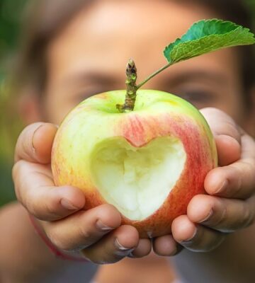 Photo shows a young child holding up an apple with a heart carved into it