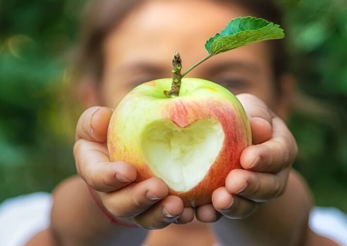 Photo shows a young child holding up an apple with a heart carved into it