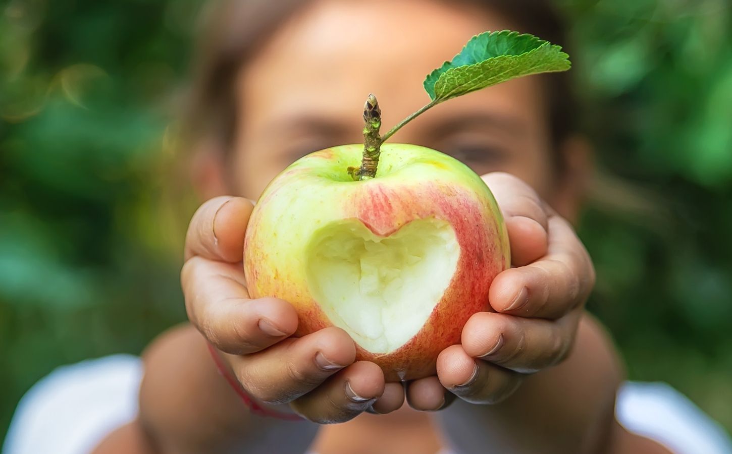 Photo shows a young child holding up an apple with a heart carved into it