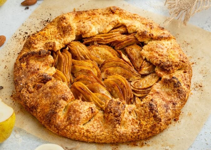 an image of an almond pear galette with slices of almond and pear surrounding the tart