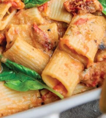 a baked hummus pasta dish with hummus, sun-dried tomatoes, tomato, rigatoni, and basil