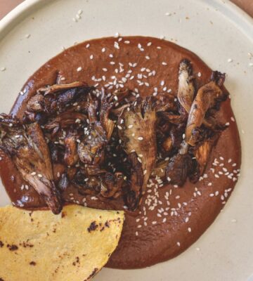 a plate of black mole with roasted oyster mushrooms served with tortilla