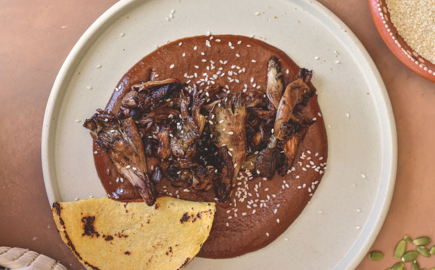 a plate of black mole with roasted oyster mushrooms served with tortilla