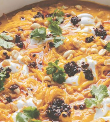 a pot of carrot noodle soup with Thai curry, peanuts, chili, chickpeas, and coriander