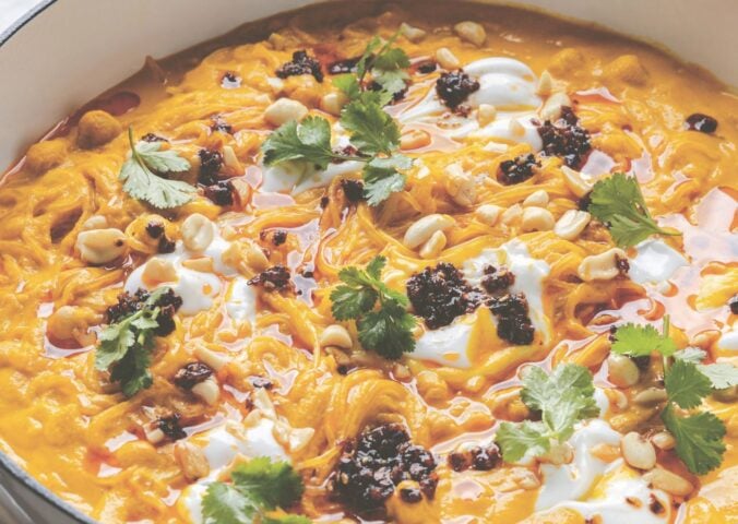 a pot of carrot noodle soup with Thai curry, peanuts, chili, chickpeas, and coriander