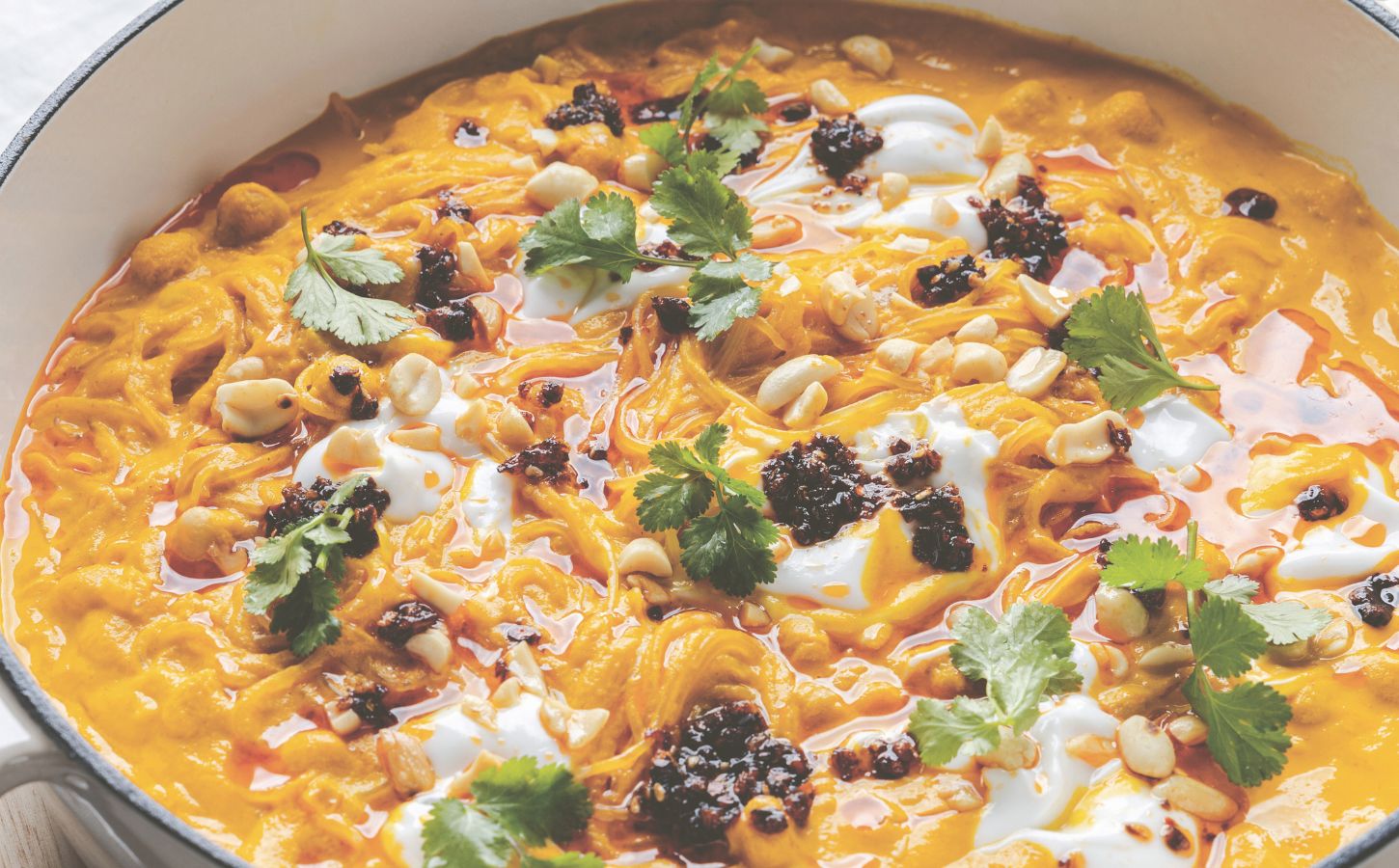 a pot of carrot noodle soup with Thai curry, peanuts, chili, chickpeas, and coriander