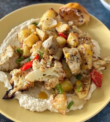 A yellow plate full of vegan cauliflower and potato bake