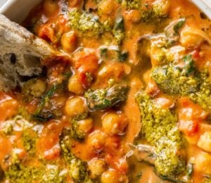 A creamy vegan pesto chickpea bowl with some crusty bread dipped in it