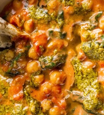 A creamy vegan pesto chickpea bowl with some crusty bread dipped in it