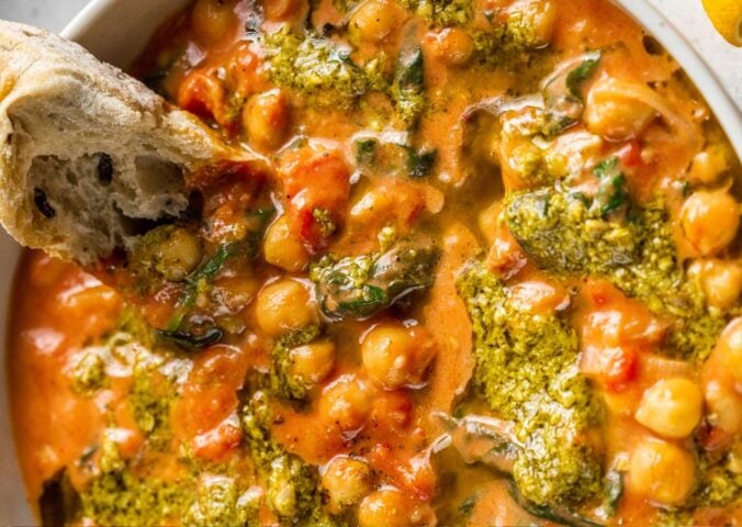 A creamy vegan pesto chickpea bowl with some crusty bread dipped in it