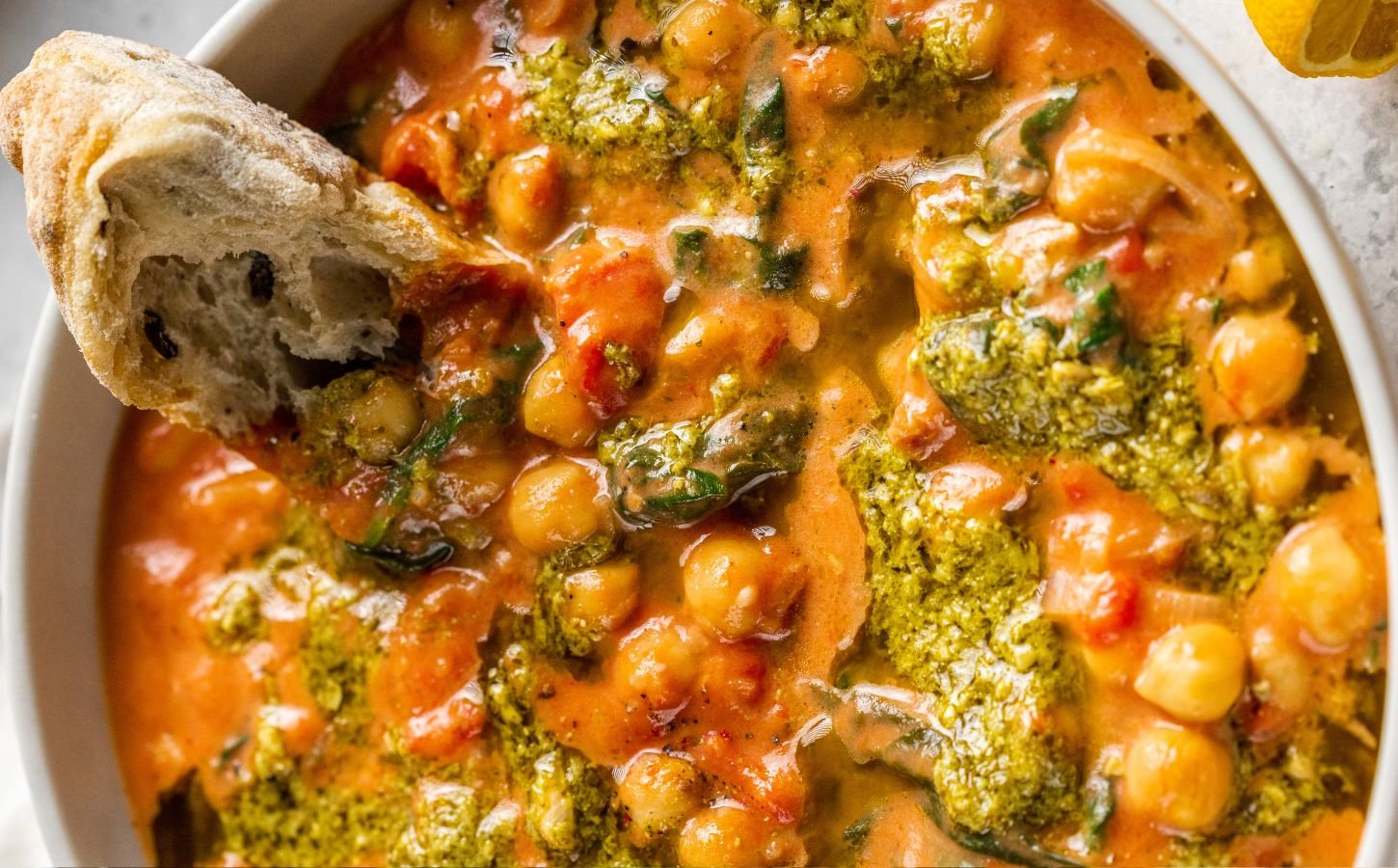 A creamy vegan pesto chickpea bowl with some crusty bread dipped in it