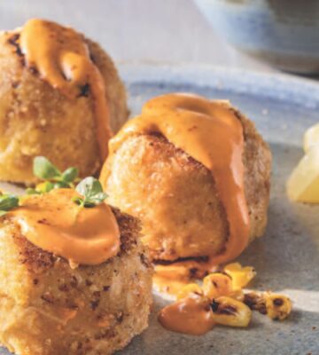 a picture of three small vegan crab cakes with spicy mayo and lemon wedges