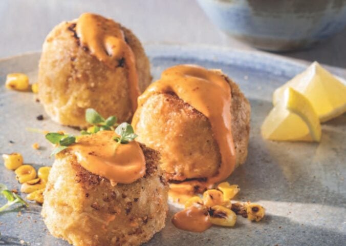 a picture of three small vegan crab cakes with spicy mayo and lemon wedges