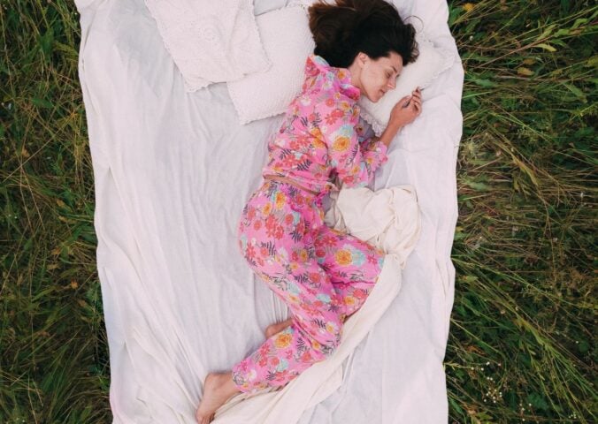 A woman in pink pyjamas lying on an Earthing sheet on the grass