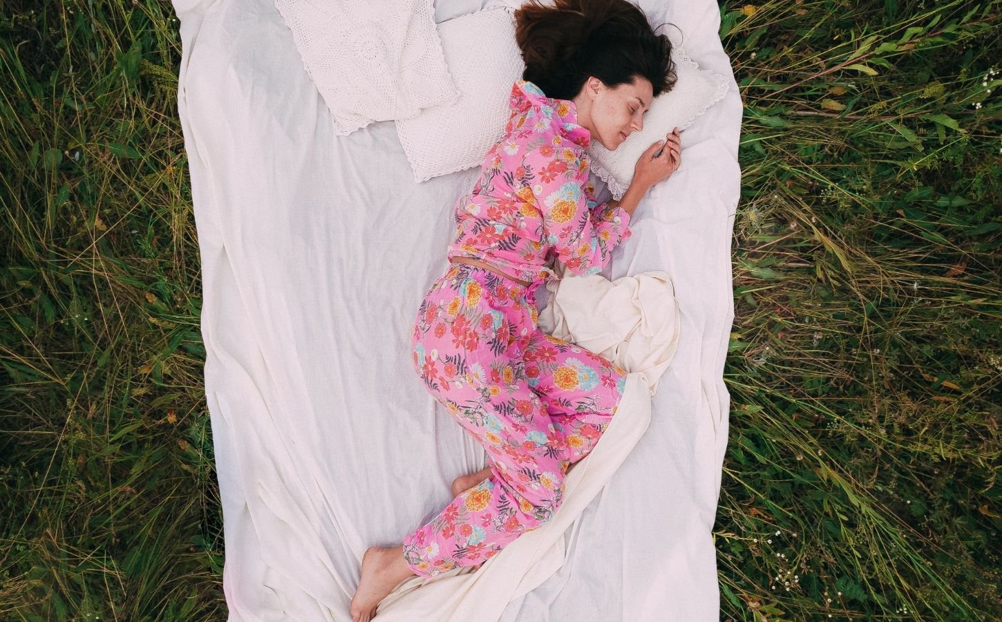 A woman in pink pyjamas lying on an Earthing sheet on the grass