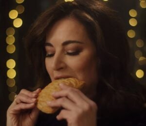 Photo shows Nigella Lawson taking a bite of a Greggs Festive Bake, which is also available as a vegan menu item