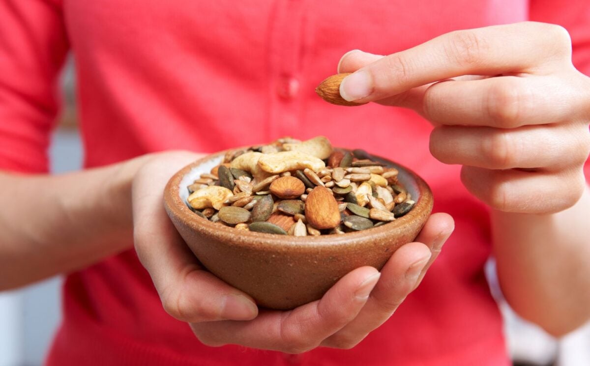 Photo shows someone eating nutritious nuts and seeds out of a wooden bowl