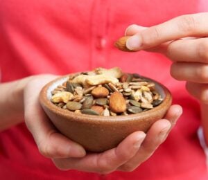 Photo shows someone eating nutritious nuts and seeds out of a wooden bowl