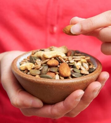 Photo shows someone eating nutritious nuts and seeds out of a wooden bowl