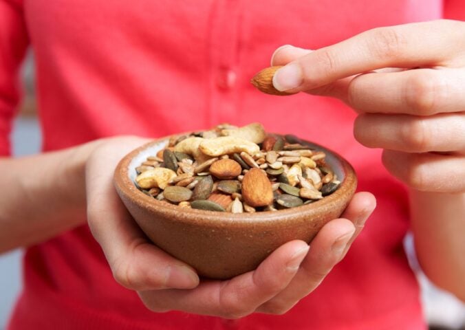 Photo shows someone eating nutritious nuts and seeds out of a wooden bowl