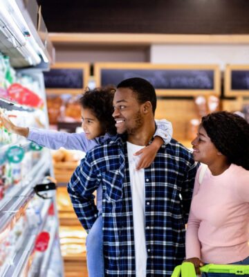 Photo shows a young family shopping in the refrigerated section of a supermarket