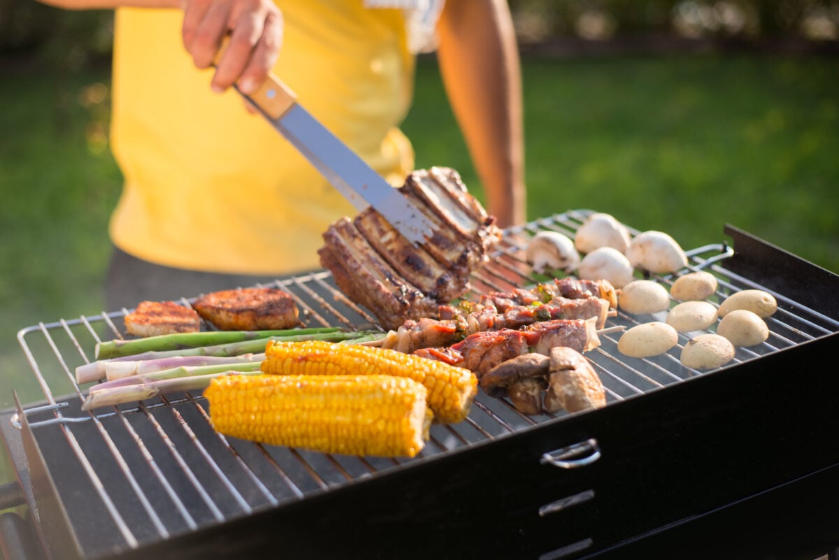 Photo shows a man grilling meat and vegetables on a BBQ