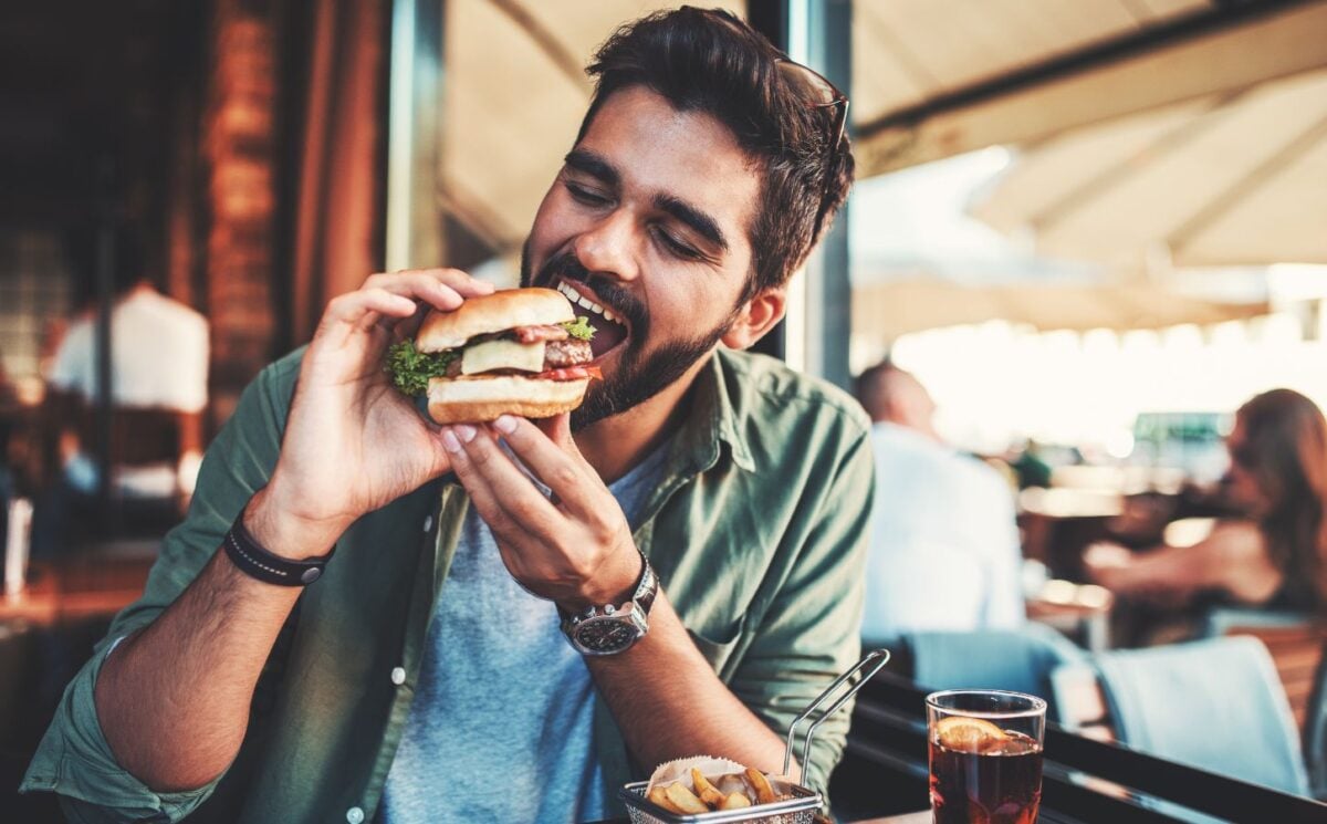 Photo shows a man just about to take a bit from a burger in a cafe