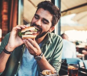 Photo shows a man just about to take a bit from a burger in a cafe