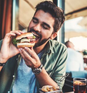 Photo shows a man just about to take a bit from a burger in a cafe