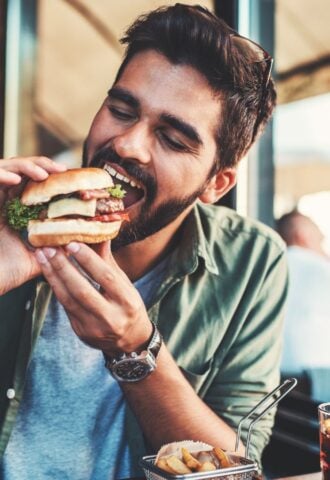 Photo shows a man just about to take a bit from a burger in a cafe