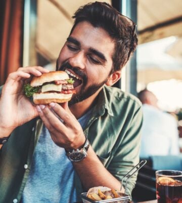 Photo shows a man just about to take a bit from a burger in a cafe