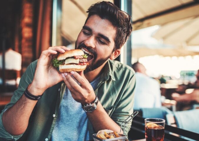 Photo shows a man just about to take a bit from a burger in a cafe