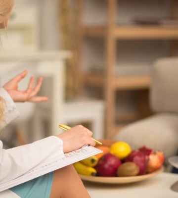 Photo shows a healthcare provider in a white coat talking to a patient with a plate of fruit and a cup of juice on the table between them