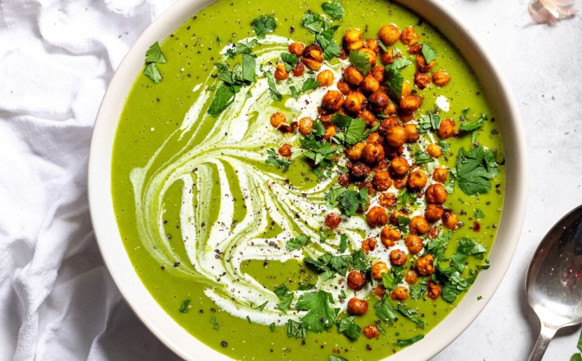 a bowl of pea and kale soup topped with vegan cream and roasted chickpeas