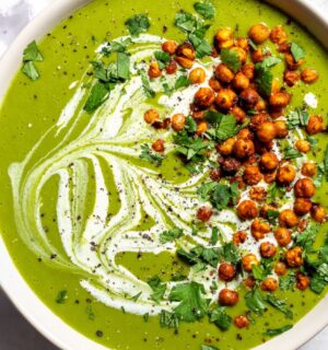 a bowl of pea and kale soup topped with vegan cream and roasted chickpeas