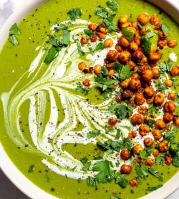 a bowl of pea and kale soup topped with vegan cream and roasted chickpeas
