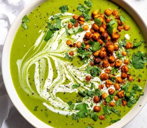 a bowl of pea and kale soup topped with vegan cream and roasted chickpeas