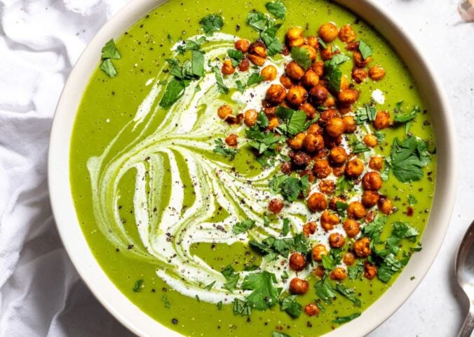 a bowl of pea and kale soup topped with vegan cream and roasted chickpeas