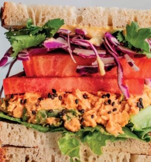 a picture of stacked peanut miso chickpea salad sandwiches with sesame, tomato, chickpea spread, and greens