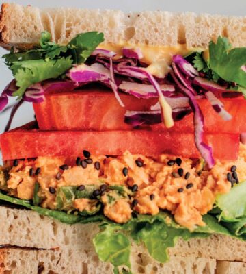 a picture of stacked peanut miso chickpea salad sandwiches with sesame, tomato, chickpea spread, and greens