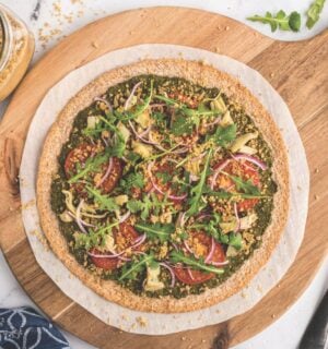 a plant-powered pesto pizza made with kale and walnut basil pesto, vegan Parmesan, tomatoes, onions, avocado, and more