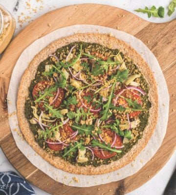 a plant-powered pesto pizza made with kale and walnut basil pesto, vegan Parmesan, tomatoes, onions, avocado, and more