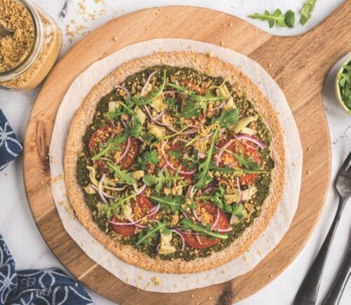 a plant-powered pesto pizza made with kale and walnut basil pesto, vegan Parmesan, tomatoes, onions, avocado, and more