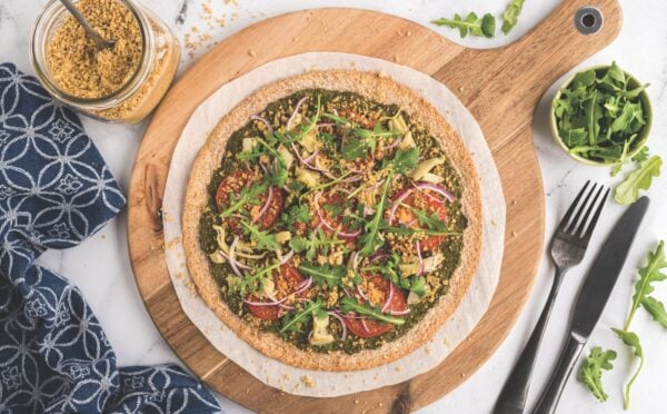 a plant-powered pesto pizza made with kale and walnut basil pesto, vegan Parmesan, tomatoes, onions, avocado, and more