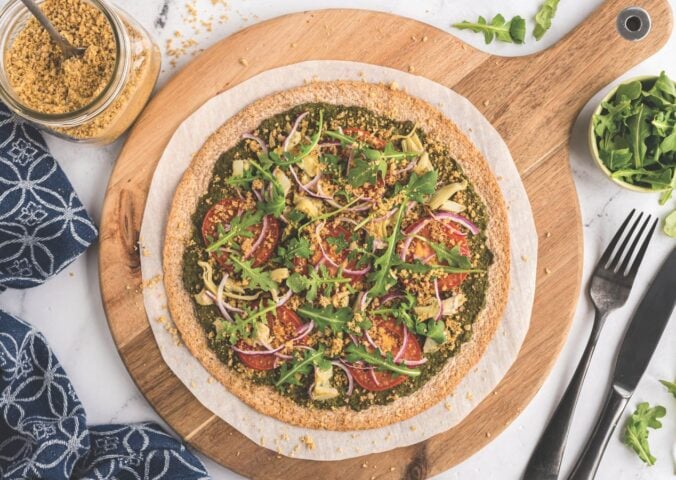 a plant-powered pesto pizza made with kale and walnut basil pesto, vegan Parmesan, tomatoes, onions, avocado, and more