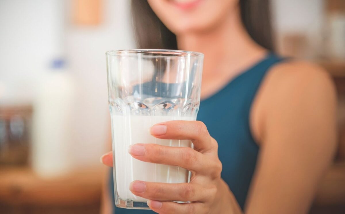 Photo shows a woman holding up a glass half full of milk