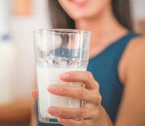 Photo shows a woman holding up a glass half full of milk