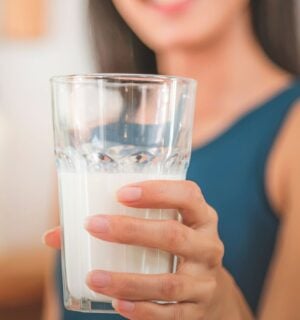 Photo shows a woman holding up a glass half full of milk